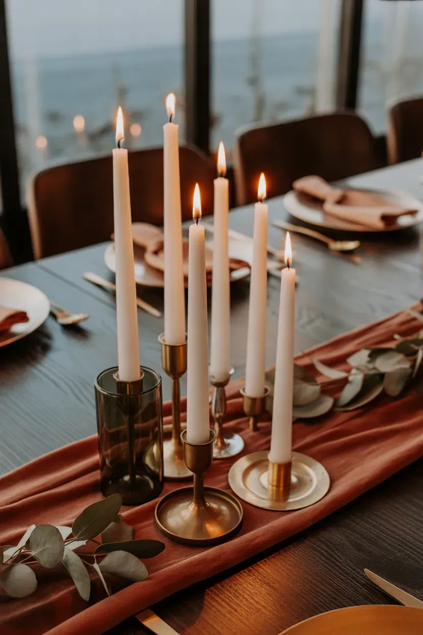 Staggered ivory taper candles in brass holders glowing on a dark Thanksgiving table